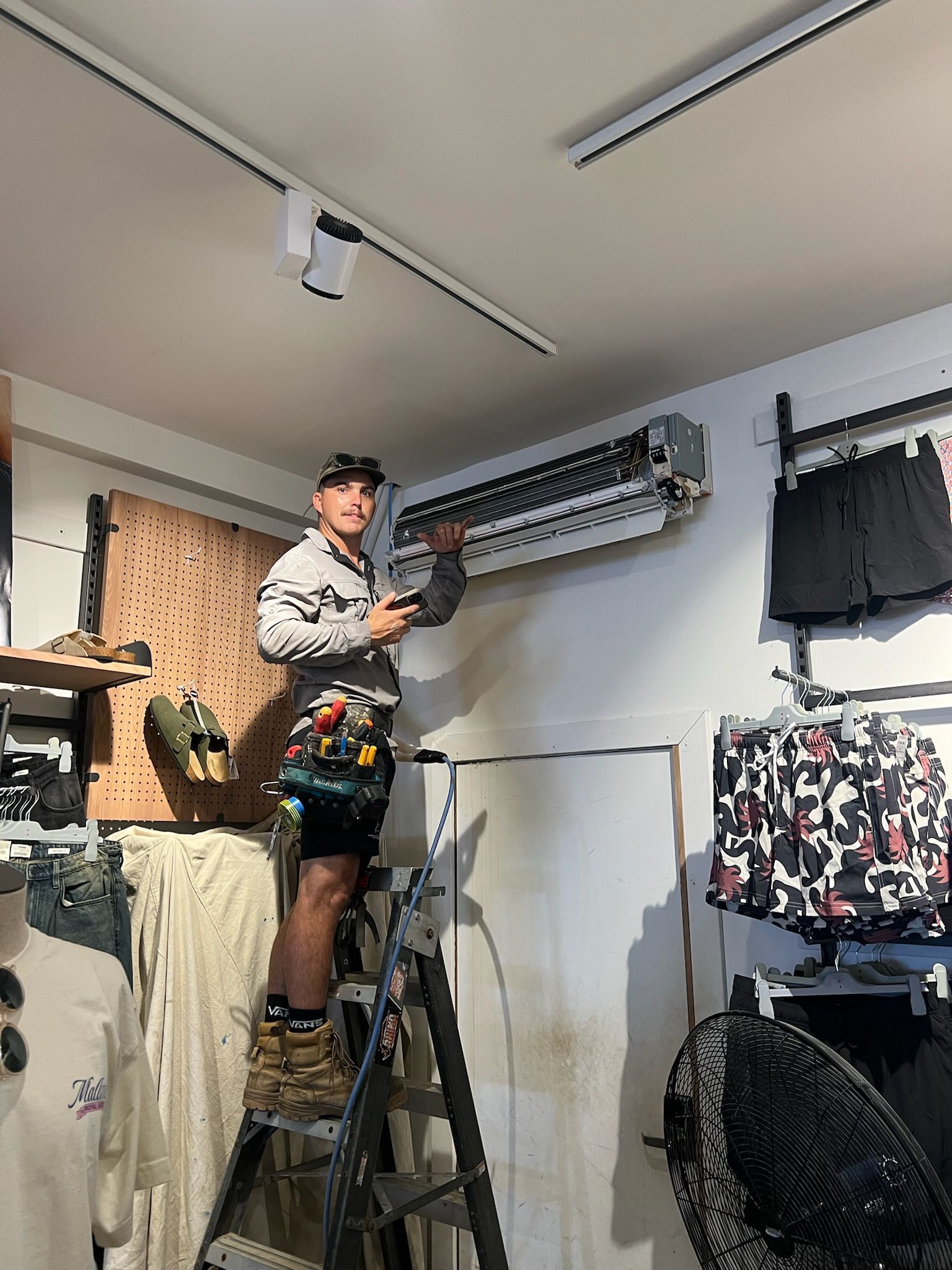 A Man is Standing on a Ladder Fixing an Air Conditioner in a Store — Kilowatts & Cool Whitsundays In Strathdickie, QLD