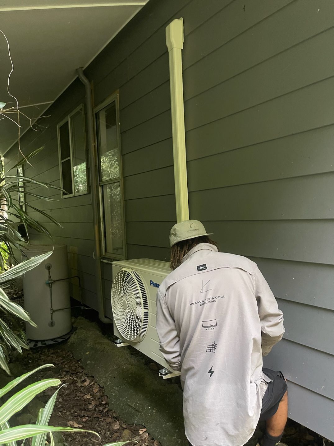 A Man is Working on an Air Conditioner Outside of a House — Kilowatts & Cool Whitsundays In Cannonvale, QLD