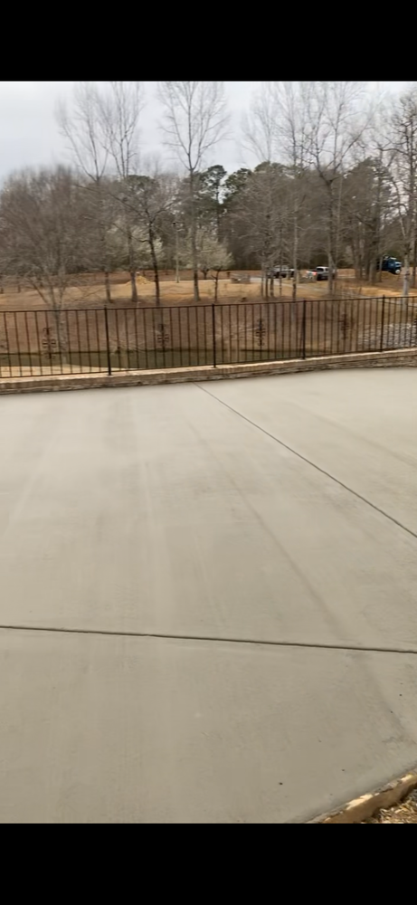 A concrete driveway with a fence and trees in the background.