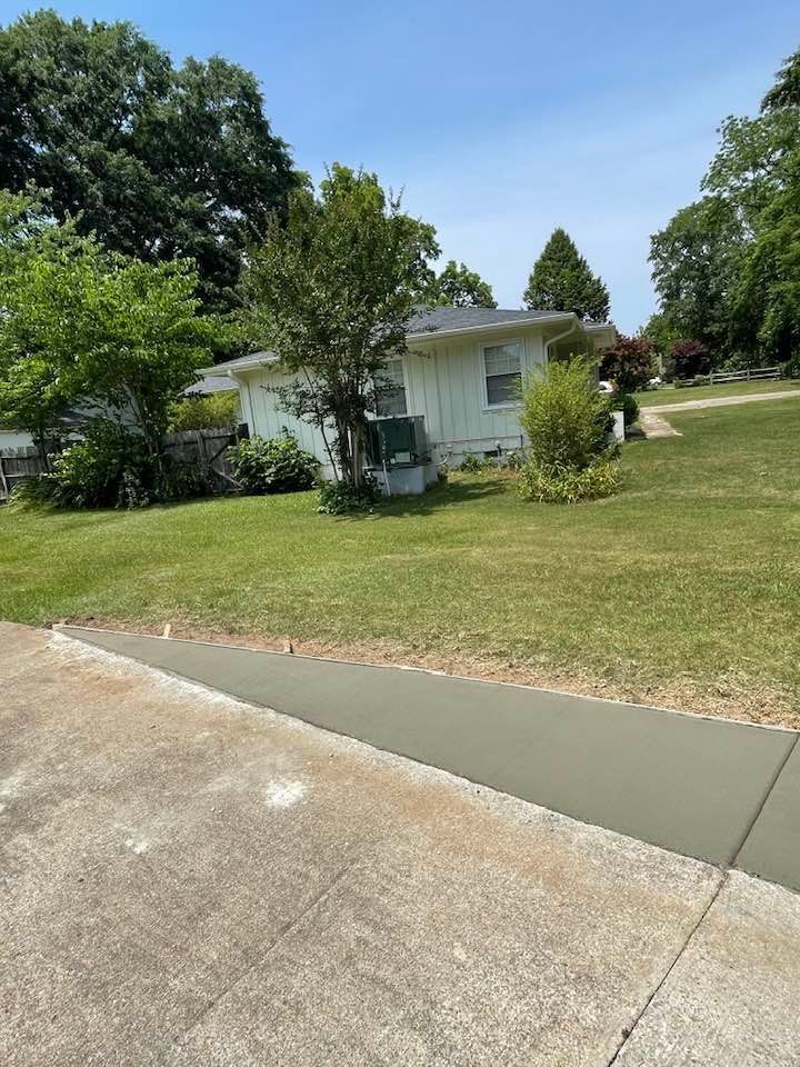 A white house is sitting on top of a lush green lawn next to a concrete driveway.