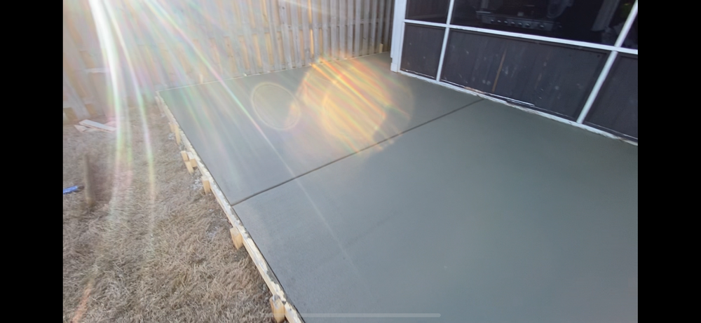 The sun is shining on a concrete sidewalk in front of a house.