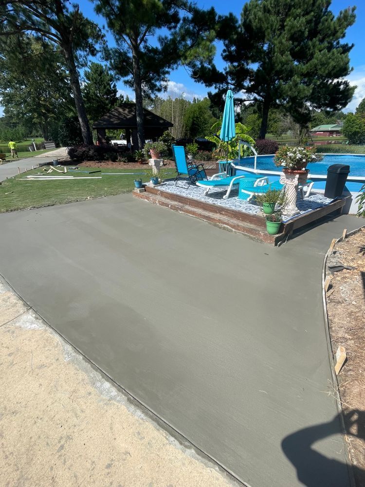 A concrete driveway leading to a pool with chairs and umbrellas.