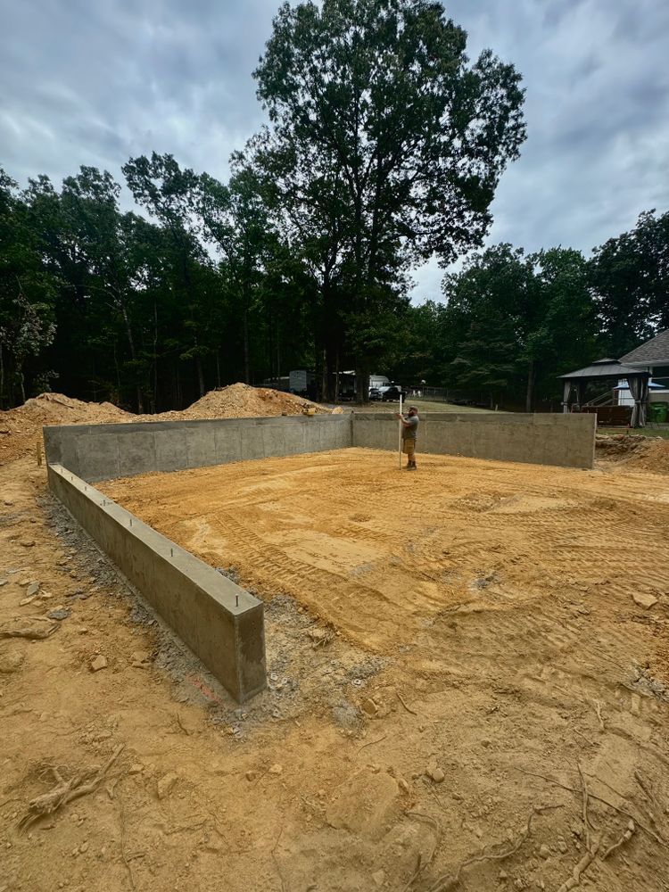 A man is standing in a dirt field next to a concrete wall.