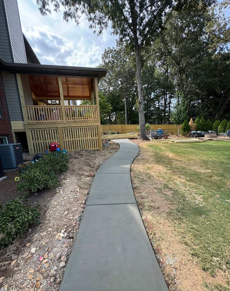 A concrete walkway leading to a house with a deck.