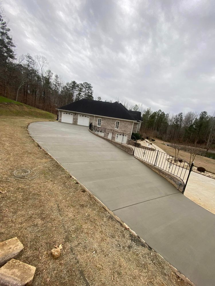 A concrete driveway leading to a house in the woods.