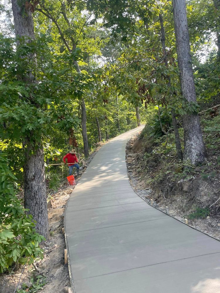 A man is walking down a concrete path in the woods.