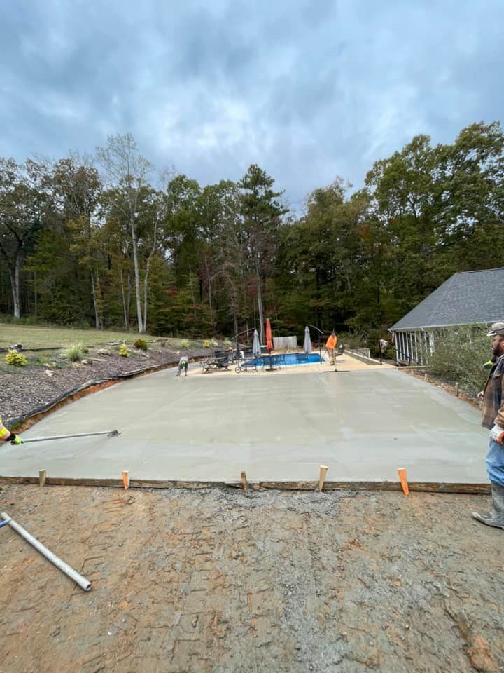 A man is standing on a concrete driveway next to a pool.