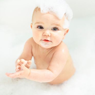 A Baby girl bathes in a bath with foam and soap bubbles