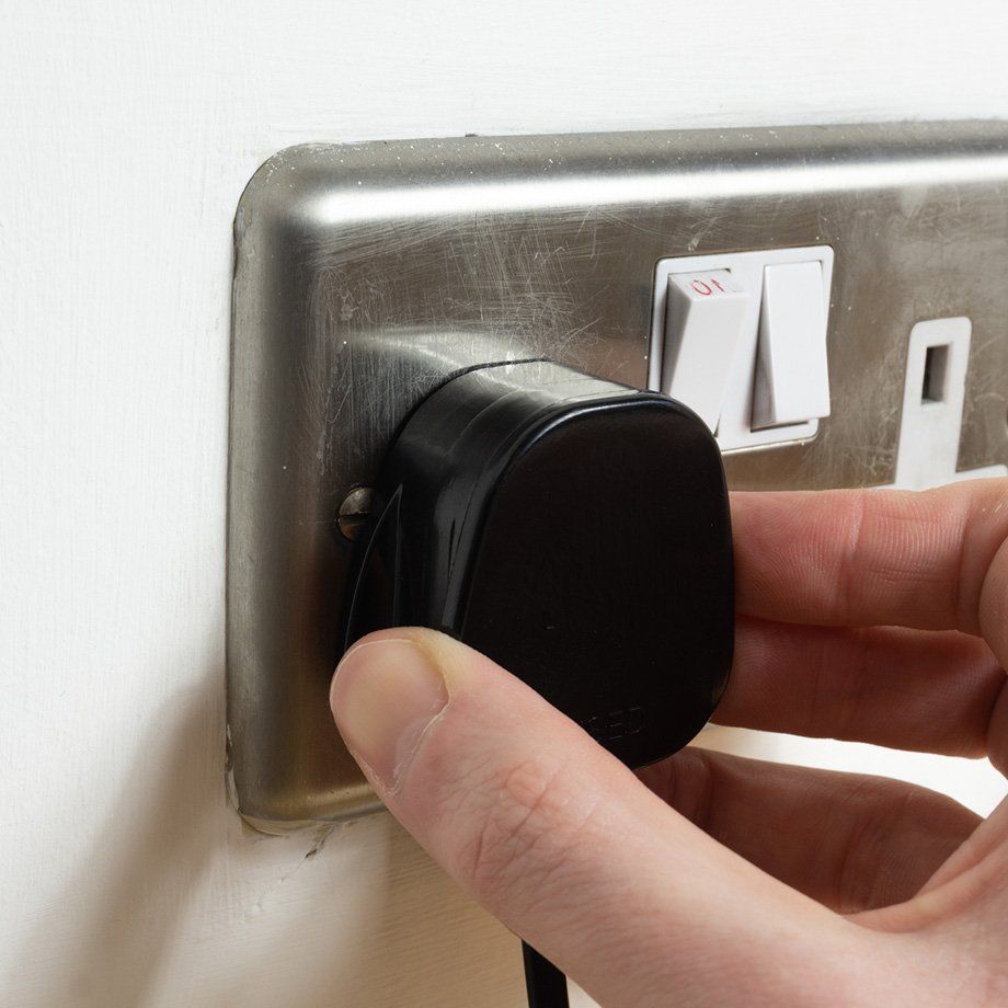 Stainless steel UK plug socket on white wall with hand plugging something in stock photo