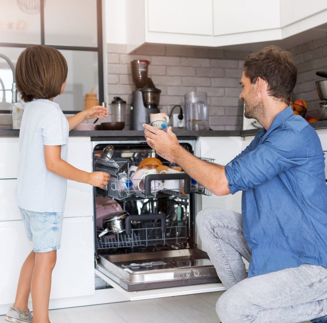 child and father filling the dishwasher