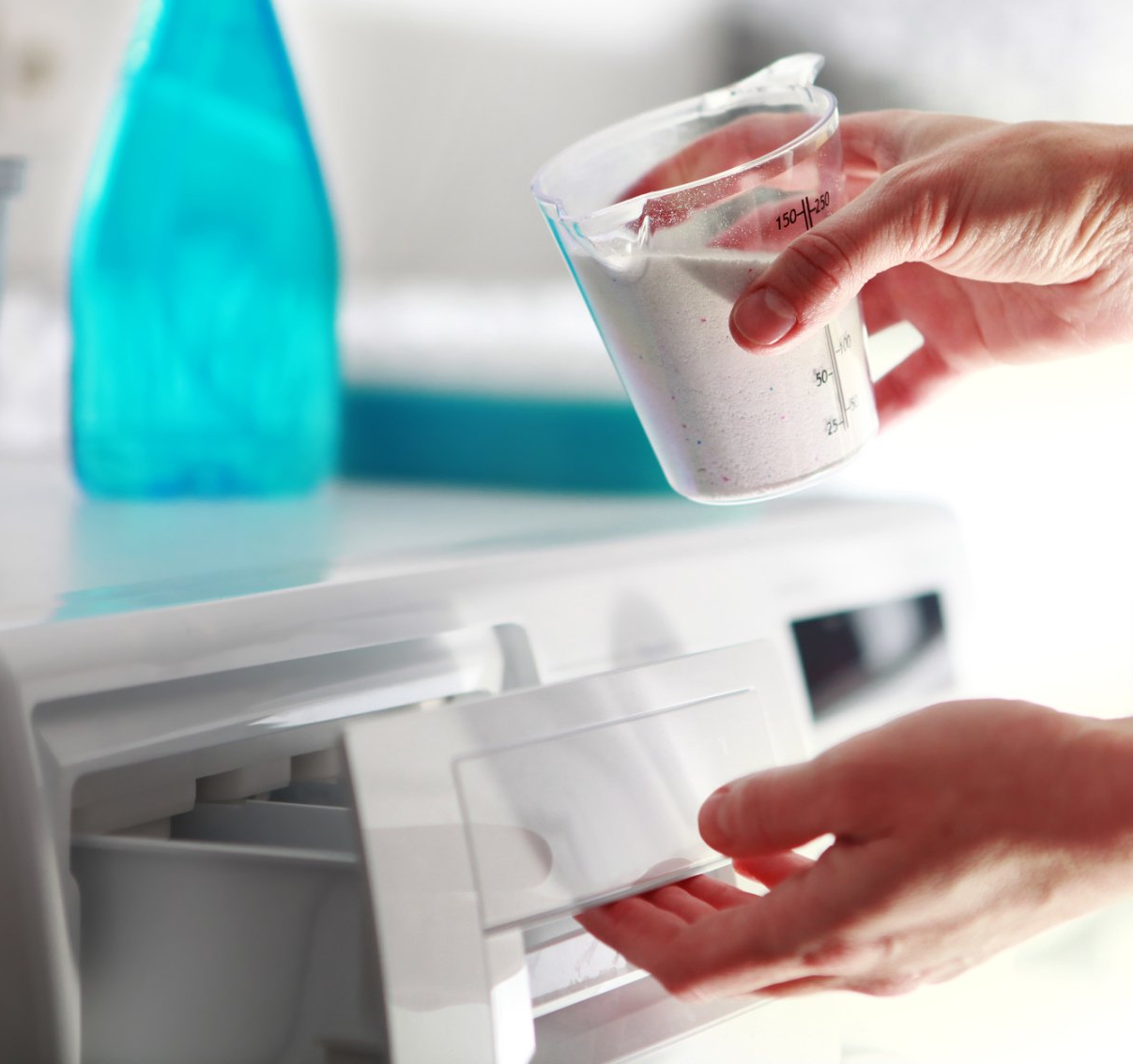 persons hands filling washing machine with laundry soap