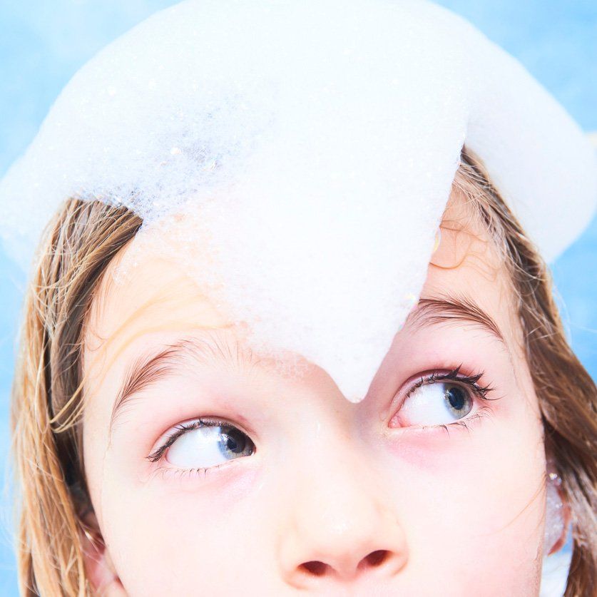 Adorable child blond girl with shampoo foam on hair taking bath.