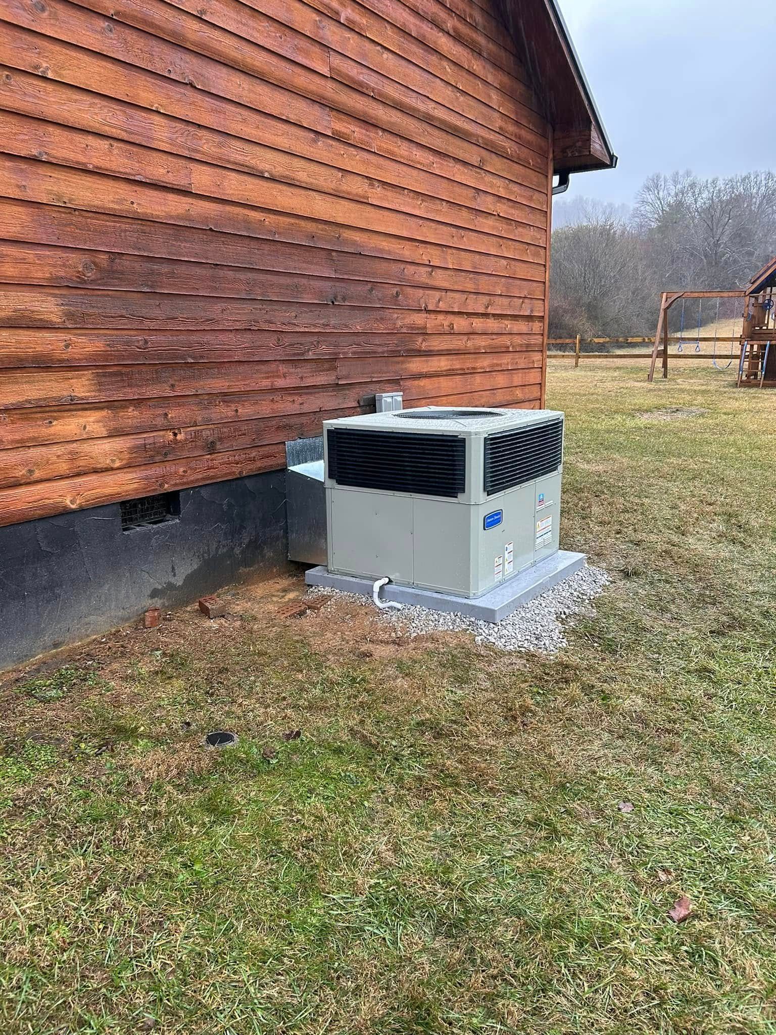 A large air conditioner is sitting in the grass next to a wooden house.