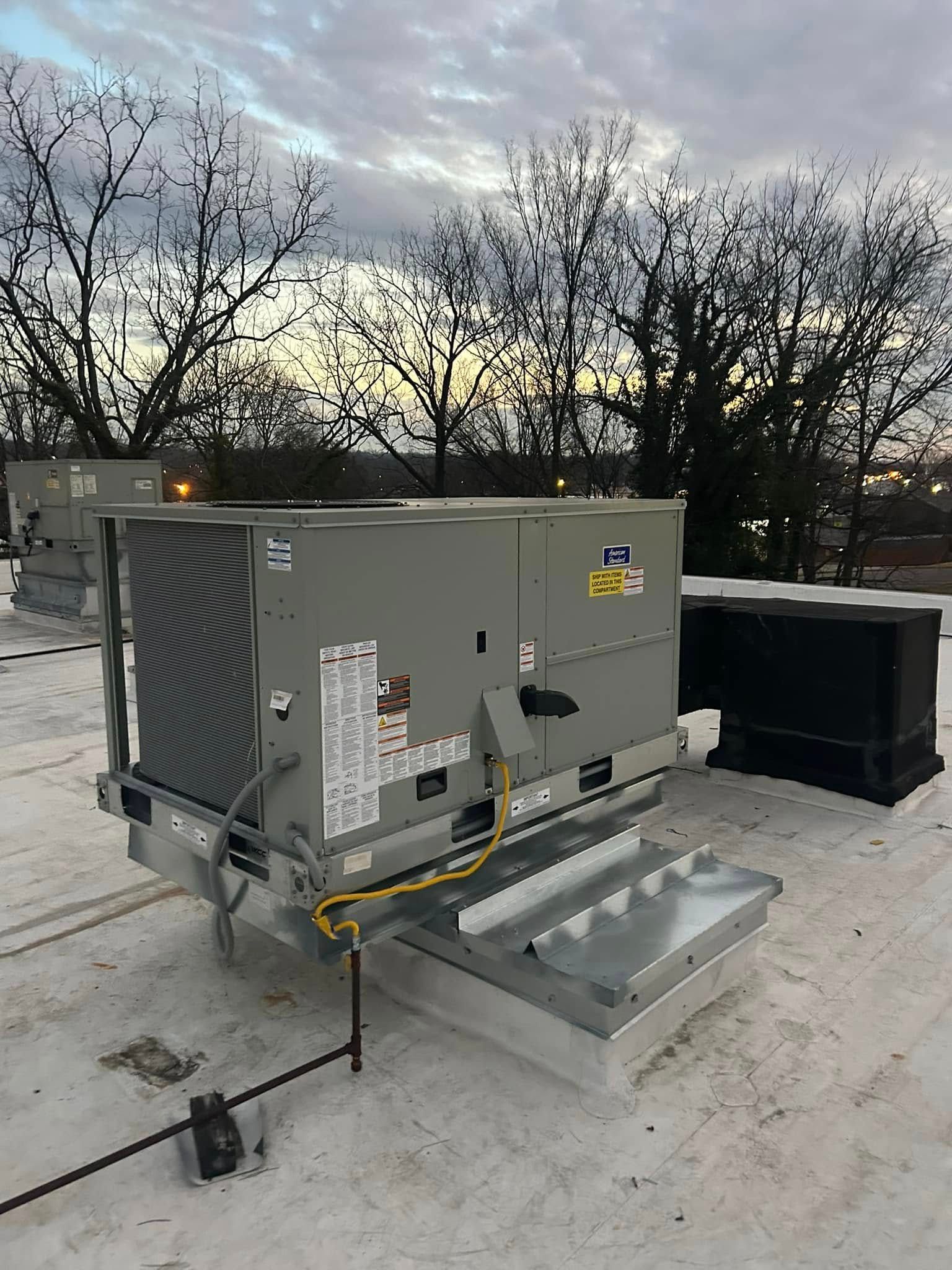 A large air conditioner is sitting on top of a snow covered roof.