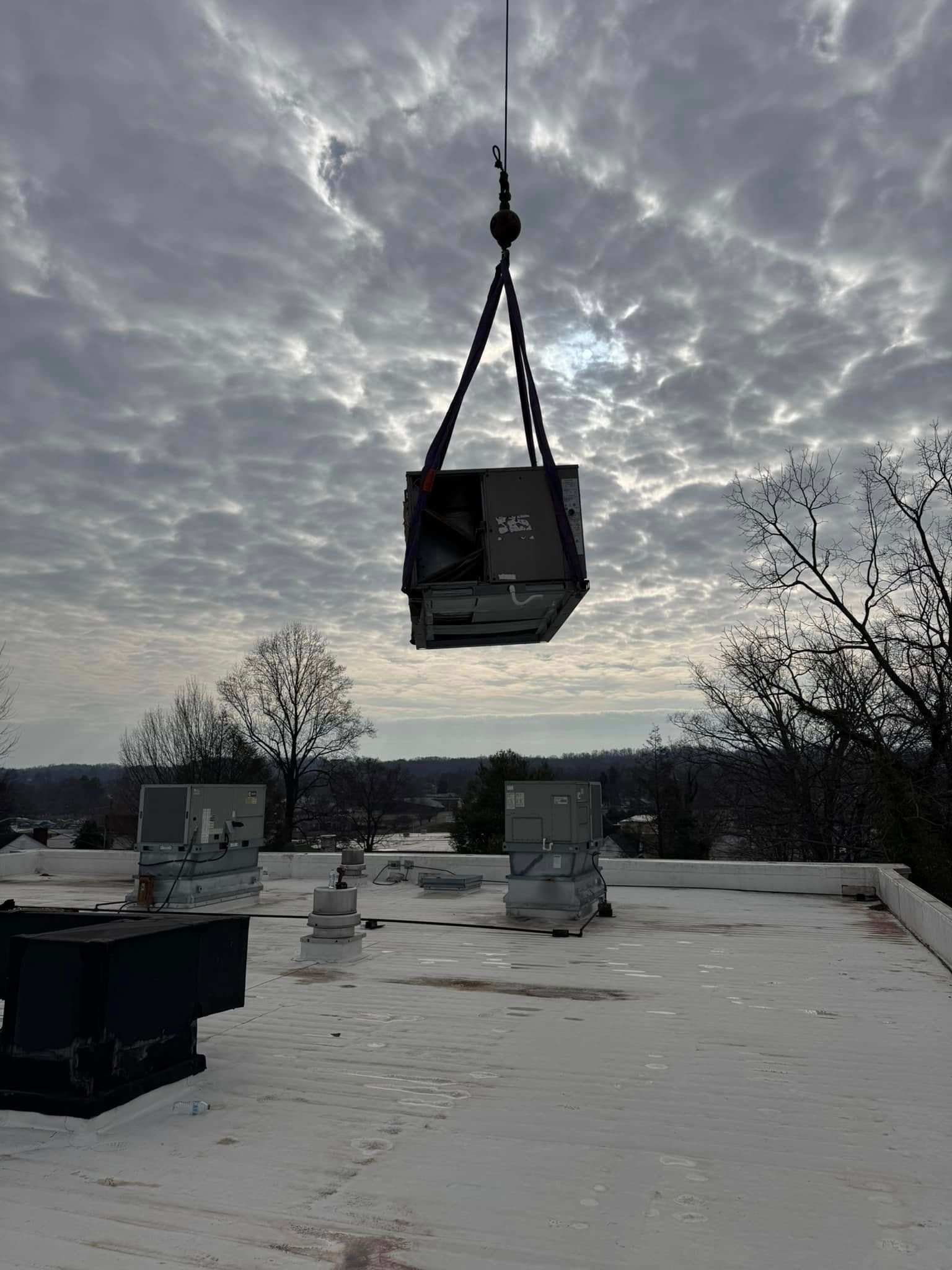 A crane is lifting an air conditioner from the roof of a building.