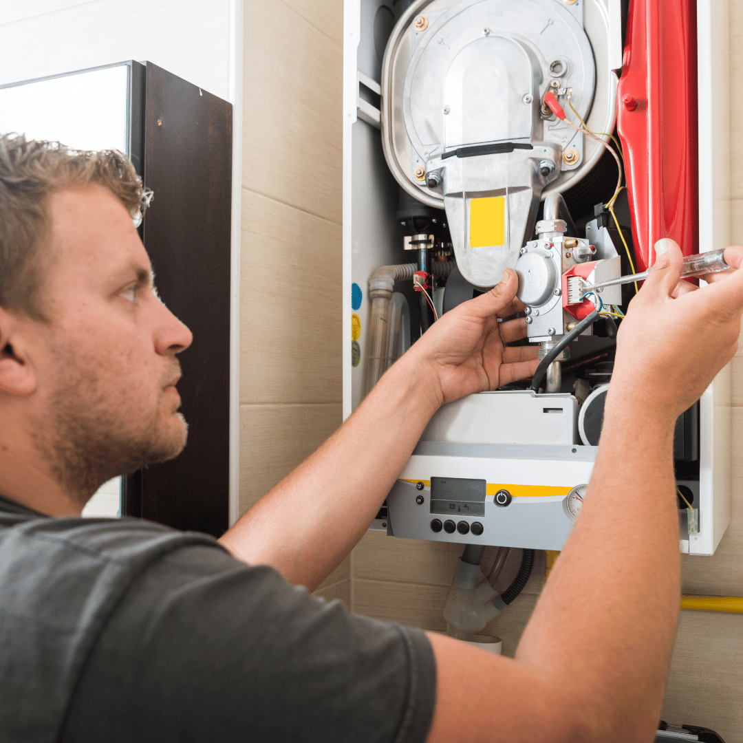 A man is working on a boiler with a screwdriver.