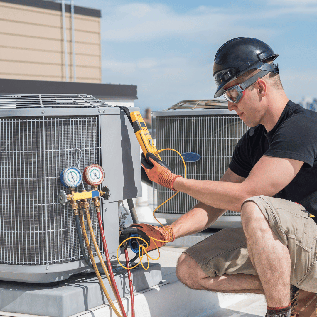 A man is working on an air conditioner on the roof of a building.
