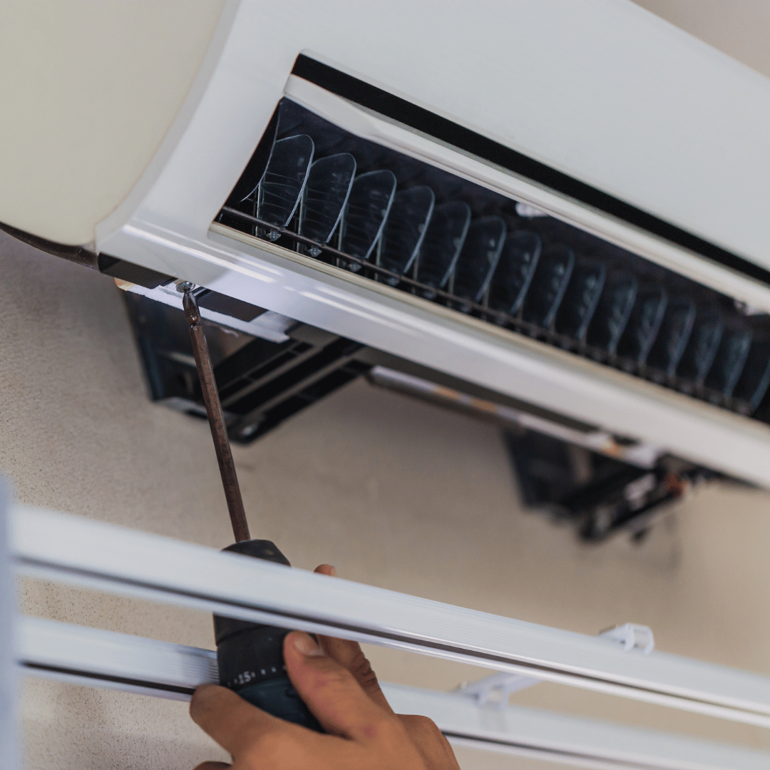 A person is fixing an air conditioner with a screwdriver.