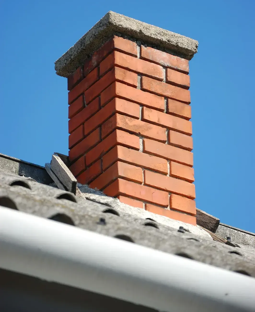 A brick chimney on top of a roof with a blue sky in the background