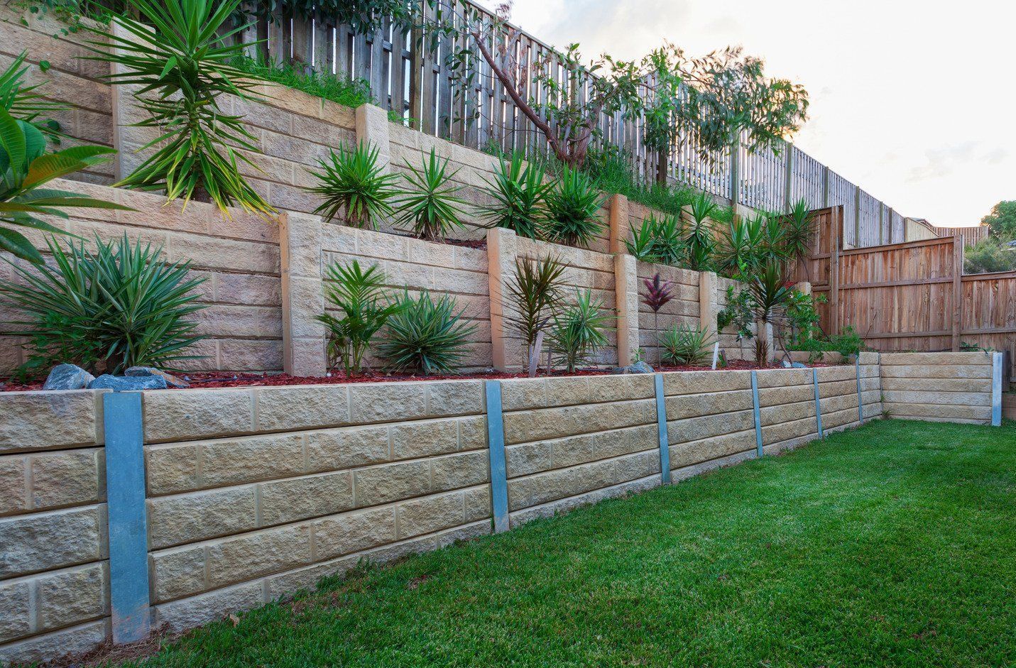 A stone wall surrounds a lush green lawn in a backyard.