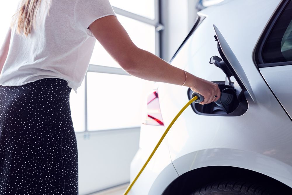 Woman Charging Electric Vehicle With Cable In Garage At Home — EV Charger Installation in Wagga Wagga