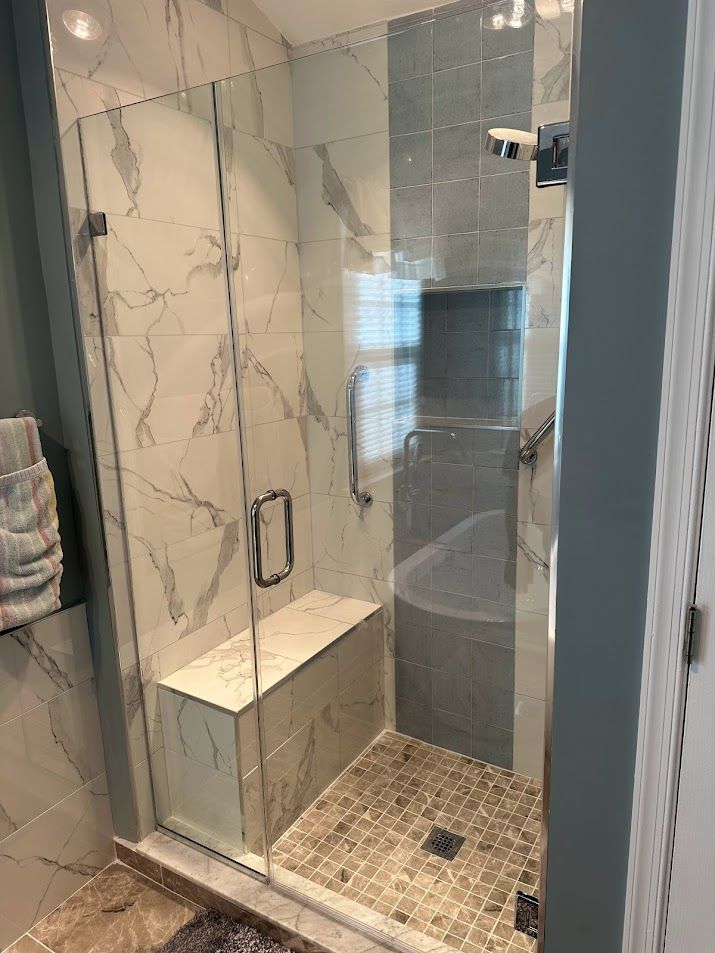 A bathroom with a walk in shower with a glass door and a bench.