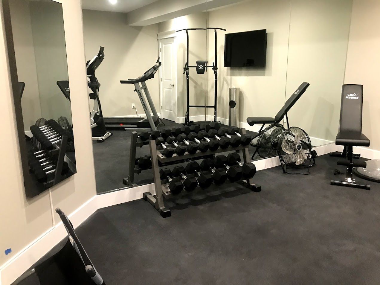 A home gym with a treadmill , dumbbells , a bench and a mirror.
