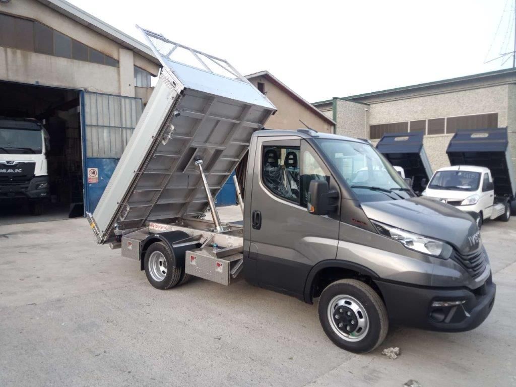 Un autocarro ribaltabile Iveco Daily grigio con il cassone sollevato in un piazzale industriale all'aperto.