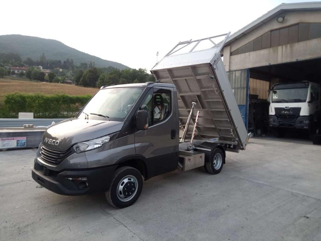 Un camion ribaltabile Iveco grigio parcheggiato fuori da un garage con il cassone parzialmente sollevato.