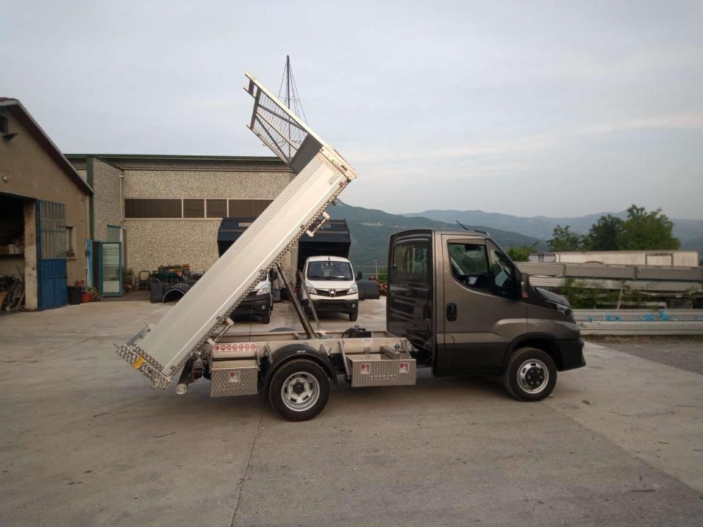 Un autocarro ribaltabile grigio parcheggiato su un piazzale asfaltato con il cassone completamente sollevato.