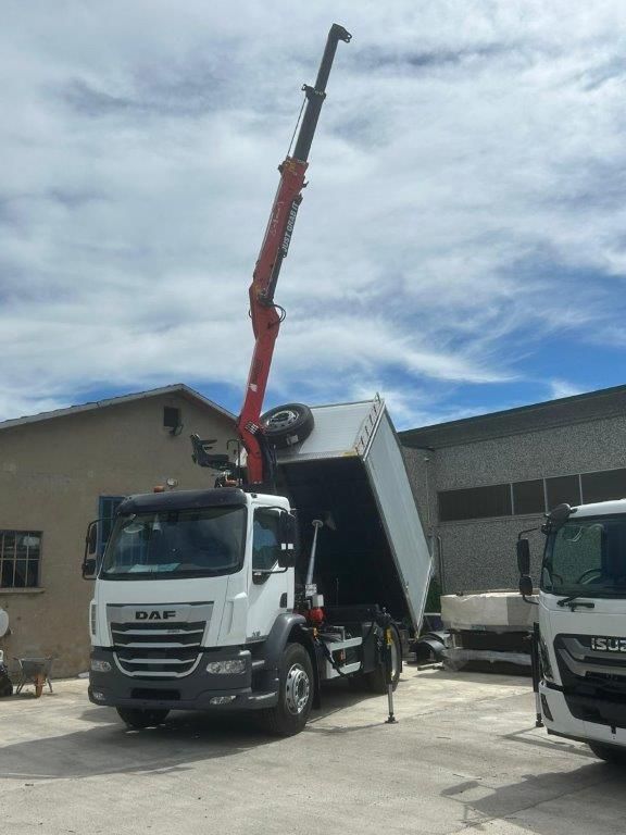 Un camion DAF bianco con una gru rossa sollevata e un cassone ribaltabile parcheggiato davanti a un edificio sotto un cielo nuvoloso.