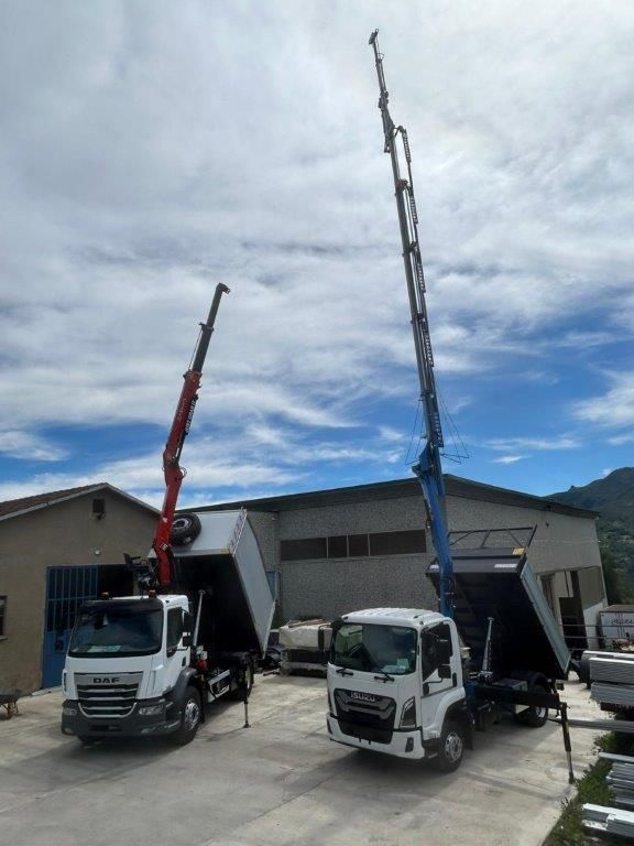 Due camion con bracci di gru idraulici sollevati erano parcheggiati davanti a un edificio sotto un cielo nuvoloso.