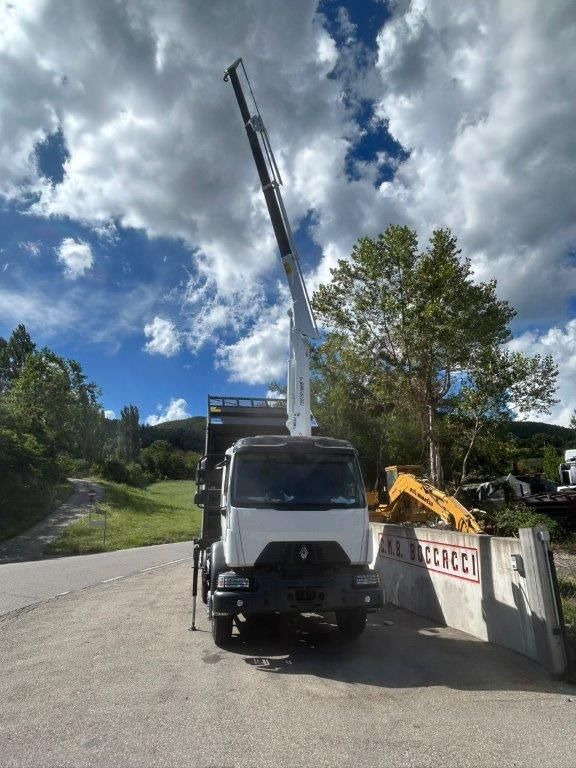 Un camion gru bianco parcheggiato su un piazzale di ghiaia vicino a un muro di cemento, stagliato contro un cielo azzurro e nuvoloso.
