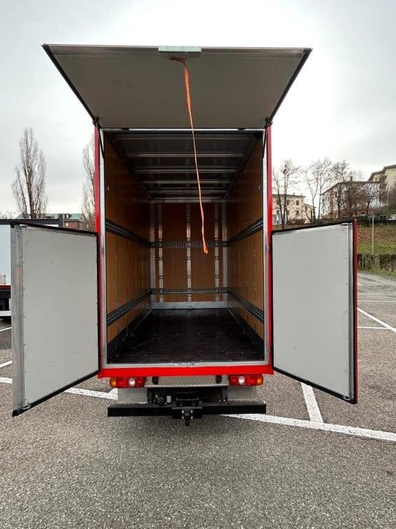 Vista posteriore di un camion rosso vuoto con le porte e il tettuccio aperti, parcheggiato in un parcheggio esterno asfaltato.