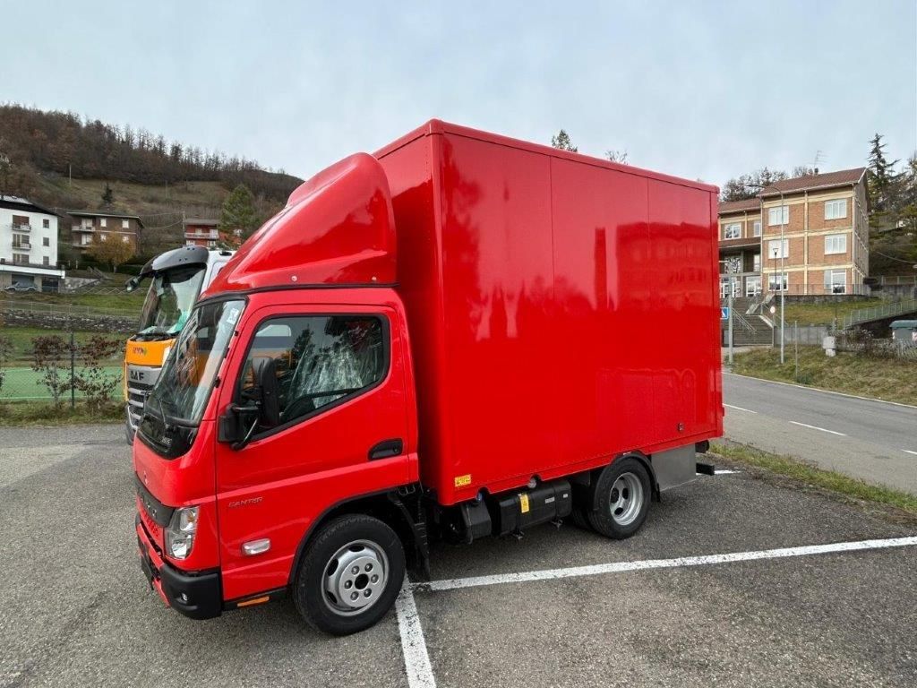 Un furgone rosso brillante parcheggiato in un parcheggio all'aperto in una giornata nuvolosa, con edifici visibili sullo sfondo.