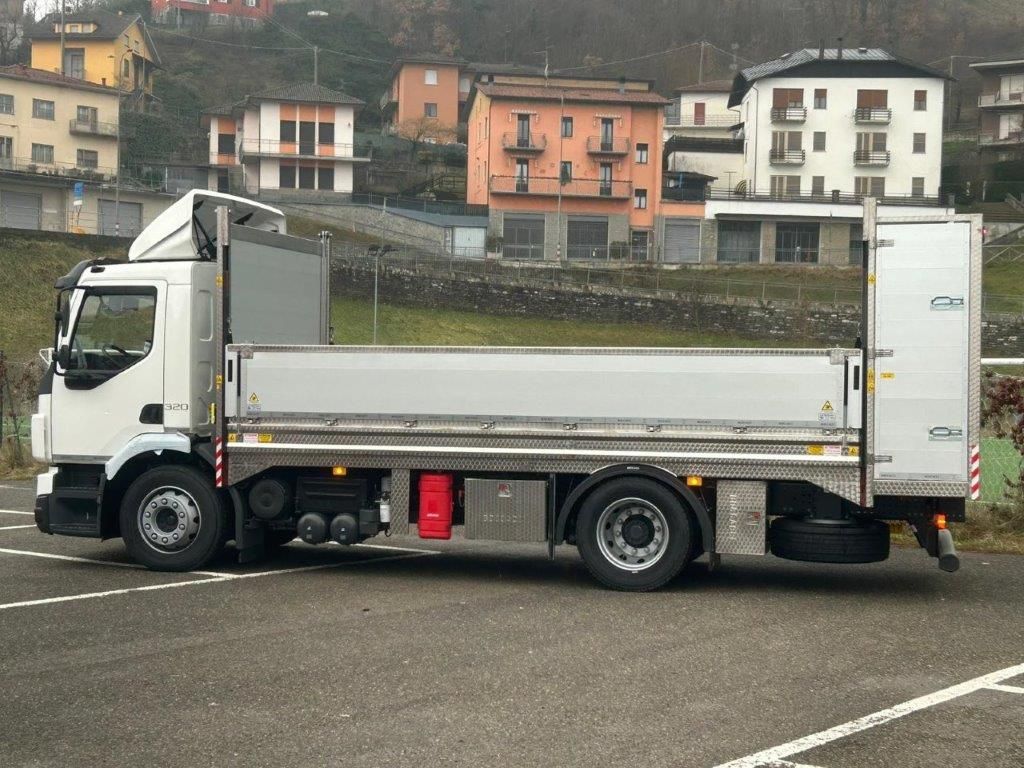 Un camioncino bianco con pianale ribassato parcheggiato in un'area di sosta all'aperto, con edifici residenziali sullo sfondo.