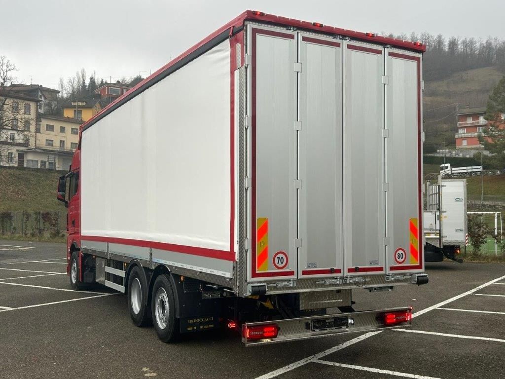Un camion rosso e argento parcheggiato in un piazzale asfaltato, visto da dietro, che mostra il suo grande cassone di carico con i lati bianchi.