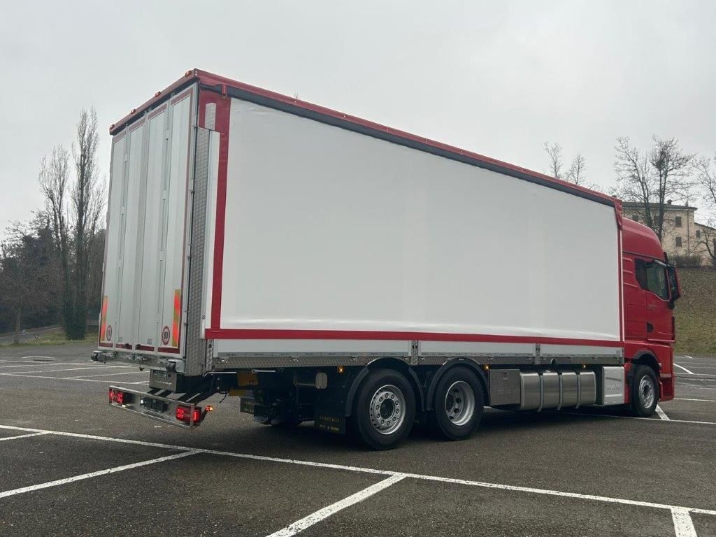 Due pick-up bianchi con cassoni ribaltabili vuoti e rialzati erano parcheggiati in un piazzale ghiaioso accanto a un grosso camion blu.
