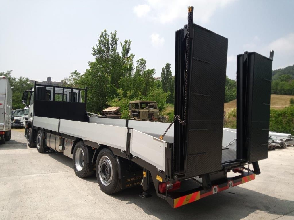 Un camioncino a pianale ribassato parcheggiato all'aperto, caratterizzato da un pianale con pannelli laterali bianchi e due rampe di carico verticali nere nella parte posteriore.