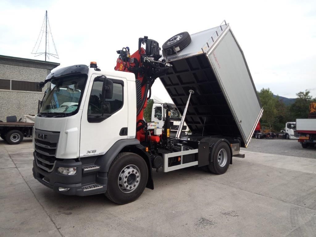 Un camion DAF bianco con una gru rossa e un container per il trasporto merci rialzato, dalle pareti argentate, parcheggiato in un'area di sosta all'aperto.