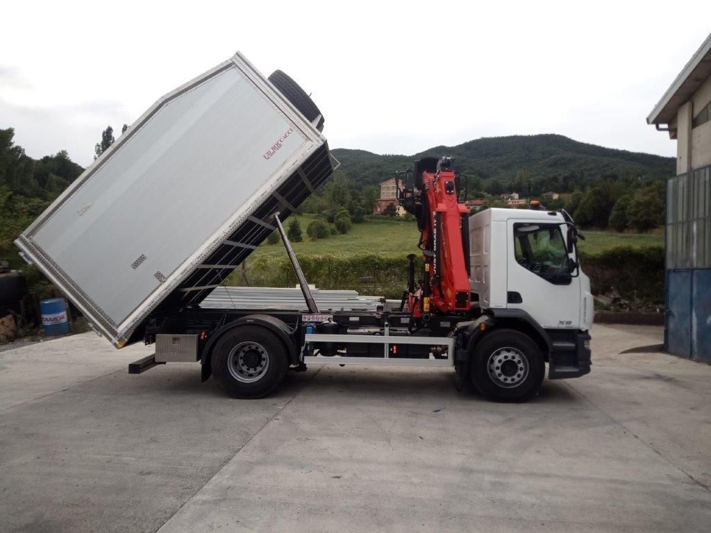 Un camion bianco con una gru rossa e un container per il carico sollevato, parcheggiato su un piazzale di cemento con uno sfondo di colline.