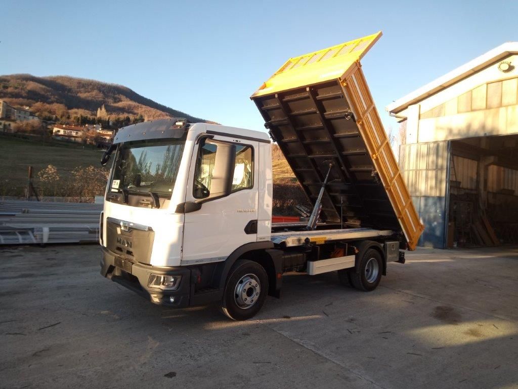 Un camion ribaltabile MAN bianco parcheggiato all'aperto con il cassone giallo inclinato in posizione sollevata.