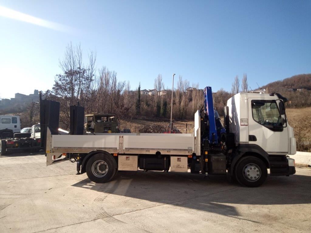 Un camioncino bianco con pianale e gru blu montata, parcheggiato su un piazzale asfaltato con uno sfondo collinare e boscoso.