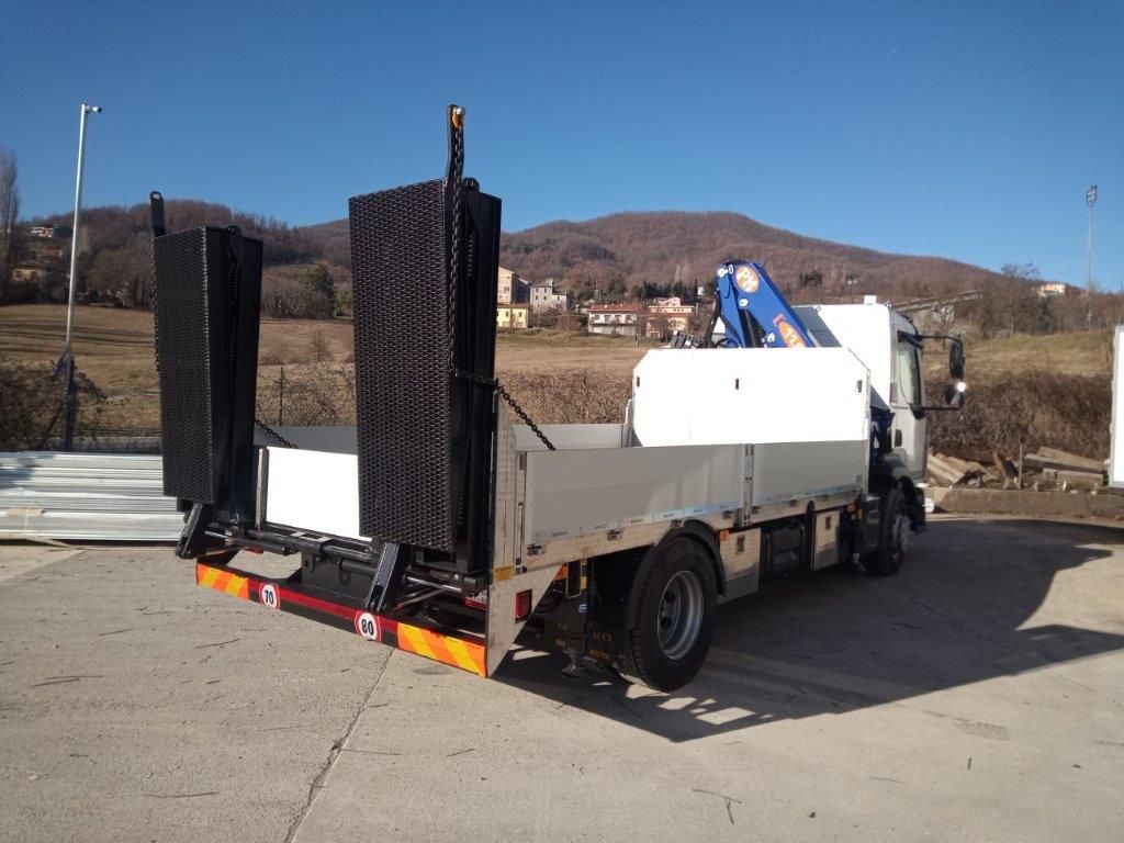 Un camion a pianale bianco con una gru idraulica e due grandi rampe di carico nere posizionate verticalmente sul retro.