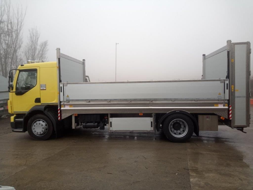 Un camion giallo con pianale di carico e sponda idraulica parcheggiato su un piazzale asfaltato in una giornata nebbiosa.