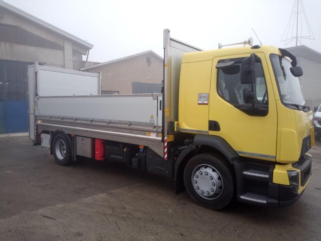 Un camioncino giallo di medie dimensioni con pianale e divisorio di carico bianco, parcheggiato in un parcheggio all'aperto in una giornata nebbiosa.