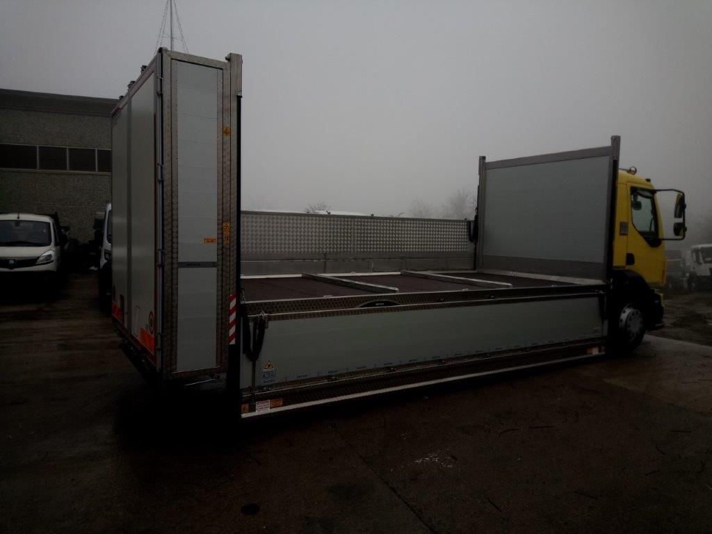 Un camioncino giallo a pianale ribassato con sponde laterali e posteriori alte, parcheggiato su un piazzale asfaltato sotto un cielo nuvoloso e coperto.