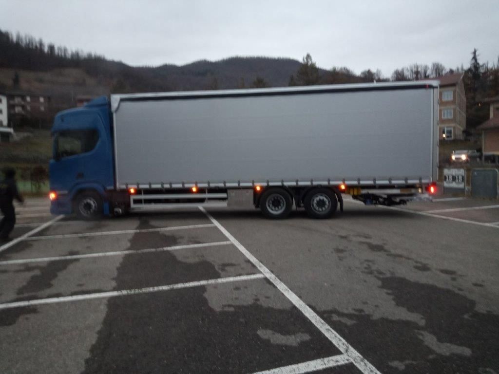 Un camion blu manovra in un parcheggio asfaltato in una giornata nuvolosa.