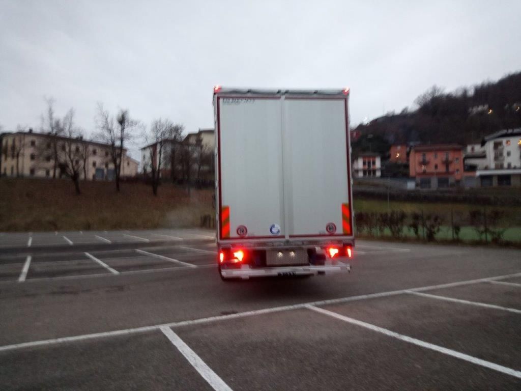 Il retro di un camioncino bianco parcheggiato in un piazzale esterno vuoto sotto un cielo nuvoloso.