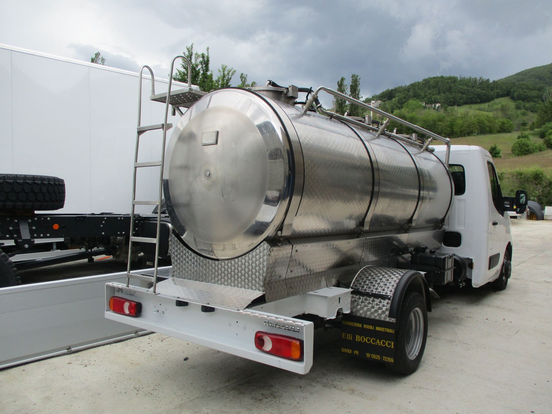 Un camion bianco con un grande serbatoio cilindrico in acciaio inossidabile parcheggiato all'aperto vicino a dolci colline verdi.